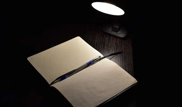 دفتر ملاحظات وقلم على سطح خشبي بإضاءة هادئة